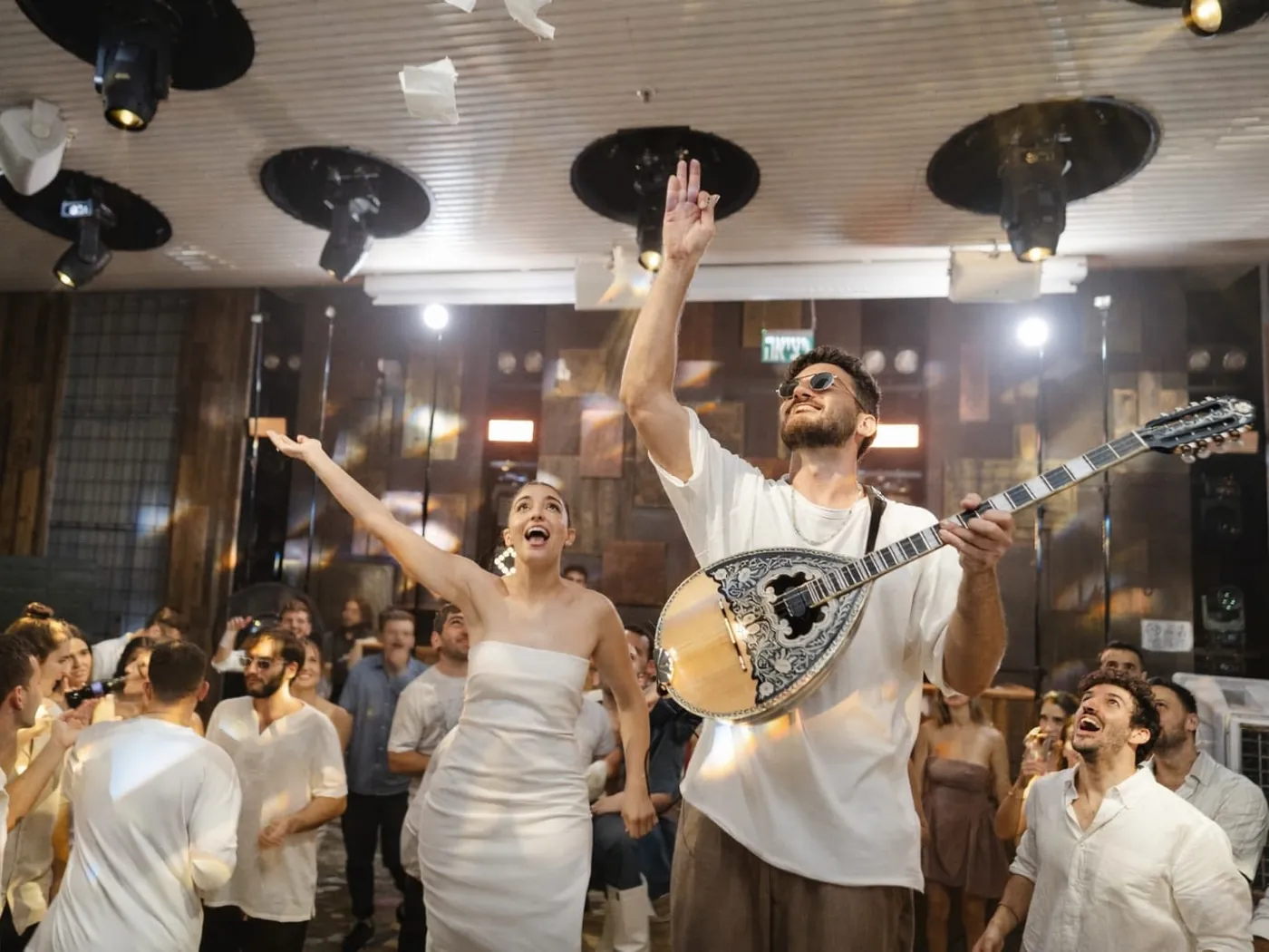 אורי מנגן בוזוקי במרכז הרחבה, הכלה מרימה ידיים לצידו והאורחים מסביב